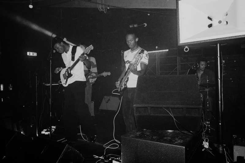 Malady live, film photo in black and white. There are 4 figures on the stage.